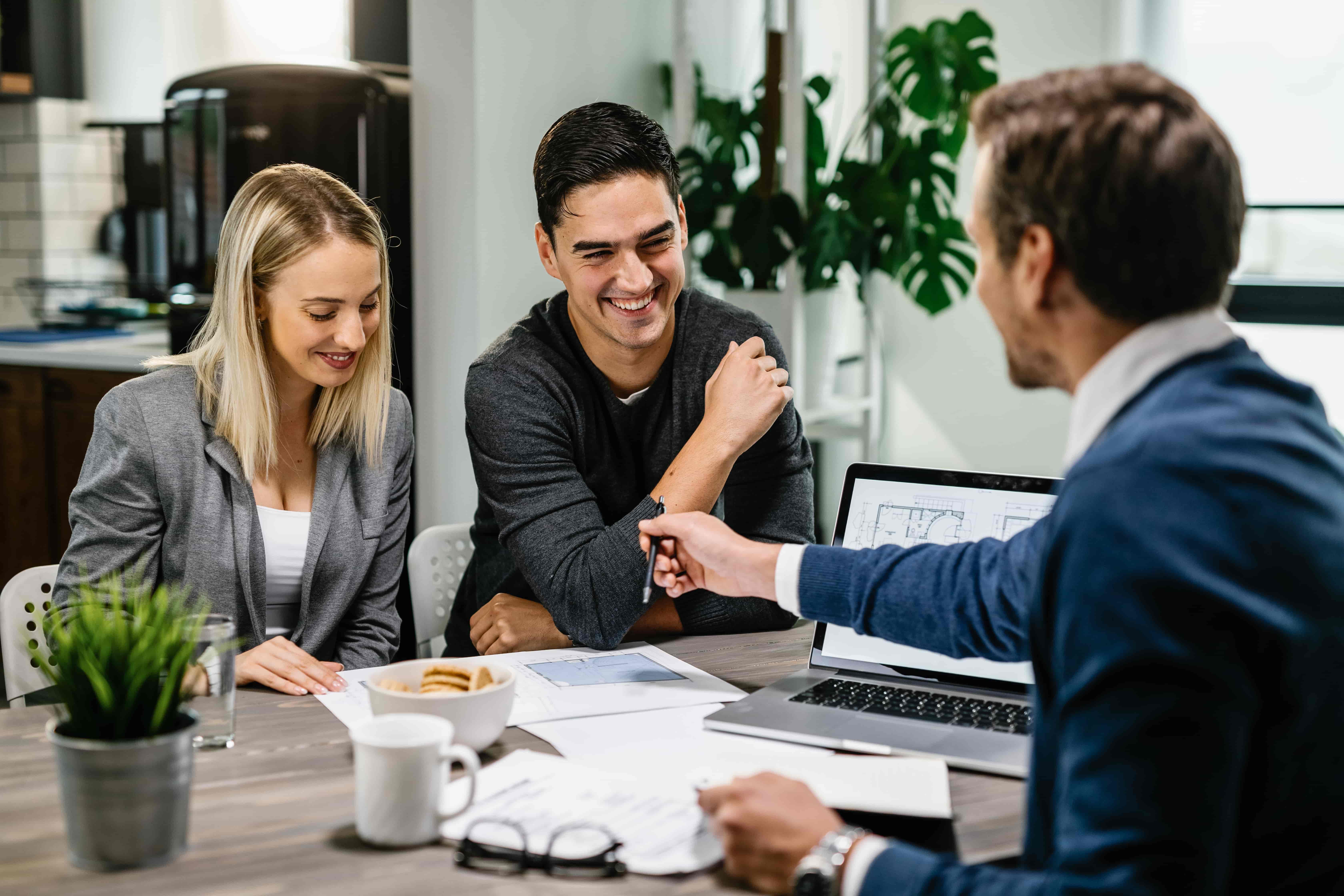 happy couple having meeting with real estate agent analyzing blueprints while communicating